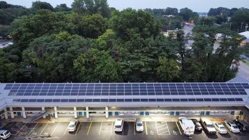 Un edificio con techo solar y un estacionamiento con varios autos.