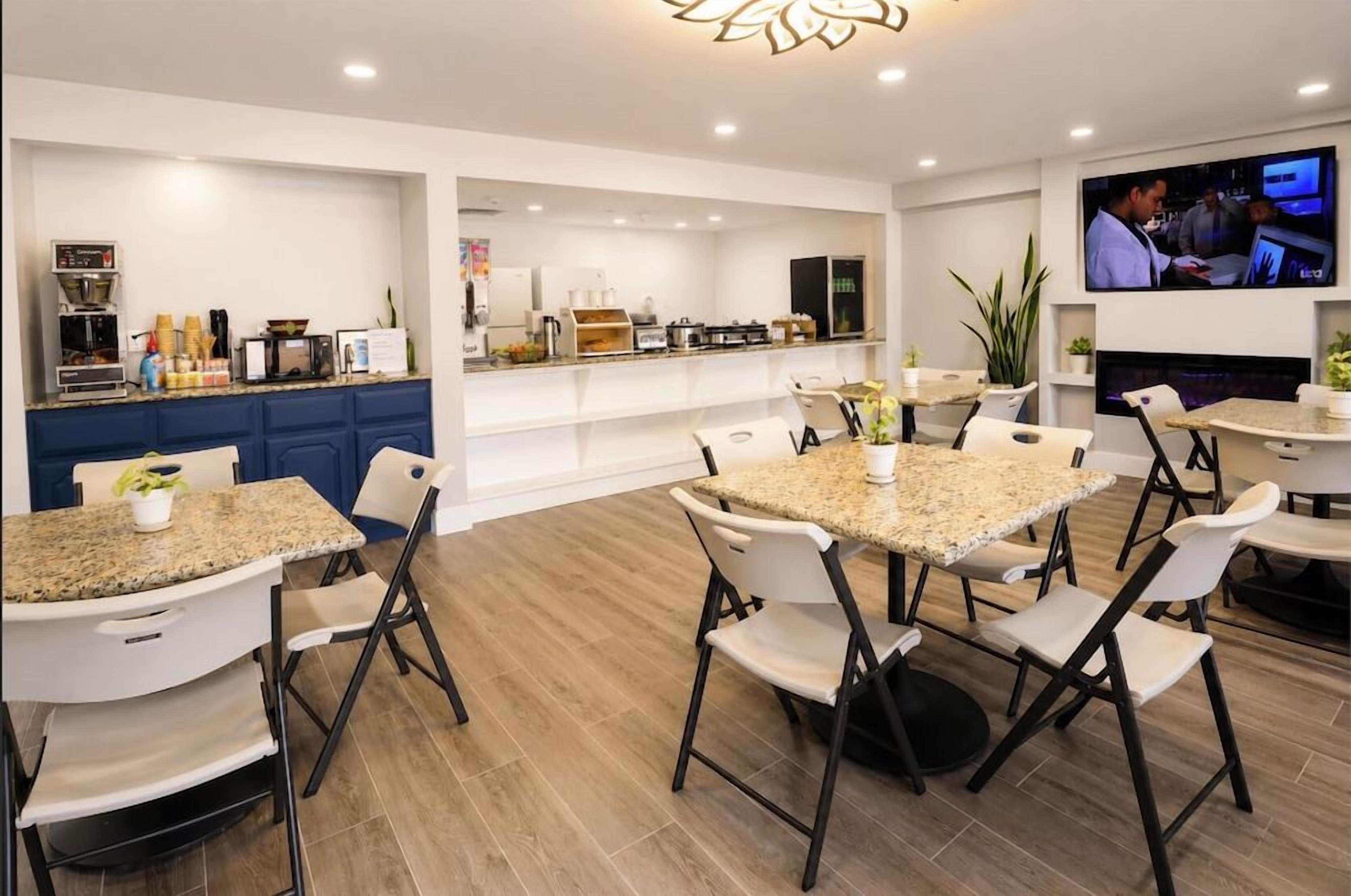 A modern dining area with multiple tables and chairs, a kitchen area with appliances, and a television screen.