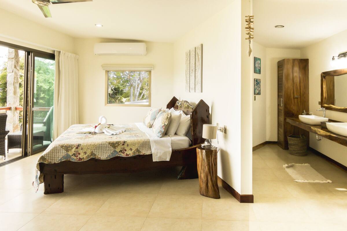 Un dormitorio con cama, mesita de noche, ventana y baño con lavabo y espejo.