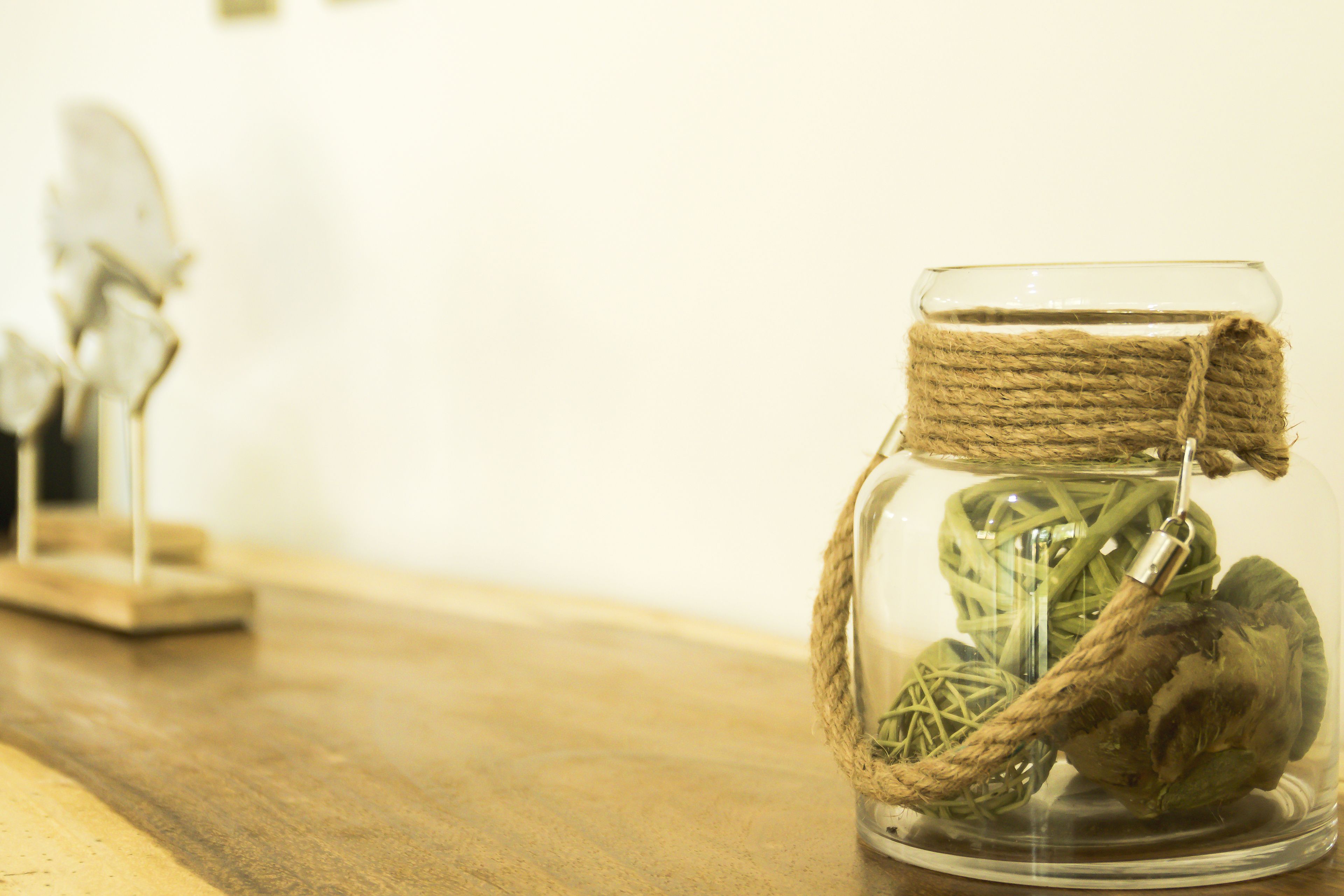 Een glazen pot met een touwen deksel, gevuld met een plant en een decoratie, op een houten ondergrond.
