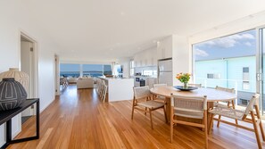 Une cuisine moderne dotée d’un îlot central, de planchers en bois et de grandes fenêtres offrant une vue sur la mer.