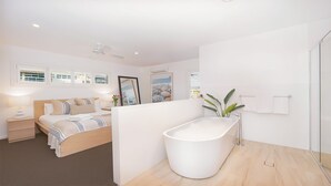 A modern bedroom with a large bed, bedside lamps, a ceiling fan, and a large window with blinds.