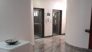 Un pasillo con suelo de mármol, dos ascensores y un mostrador de recepción con un cuenco encima.