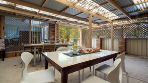 An outdoor patio with a wooden table set for dining, surrounded by white chairs.