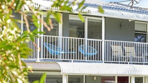 Ein zweistöckiges Gebäude mit einem Balkon, ausgestattet mit weißen Geländern und blauen Stühlen.