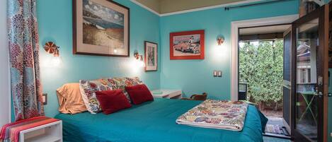 Ein Schlafzimmer mit himmelblauer Bettdecke, einem großen gerahmten Bild und einem kleinen Tisch mit Lampe.