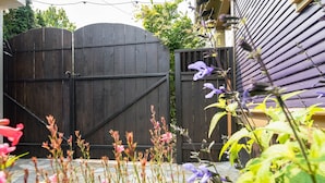 A wooden gate, a house with a dark siding exterior, and various plants in the foreground.