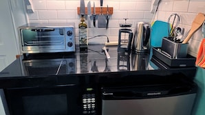 A kitchen with a black countertop, a silver toaster, a black microwave, and a stainless steel kettle.