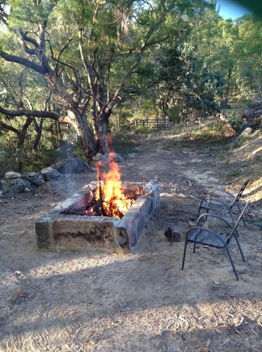 A fire pit in a natural setting with rocks and metal chairs.