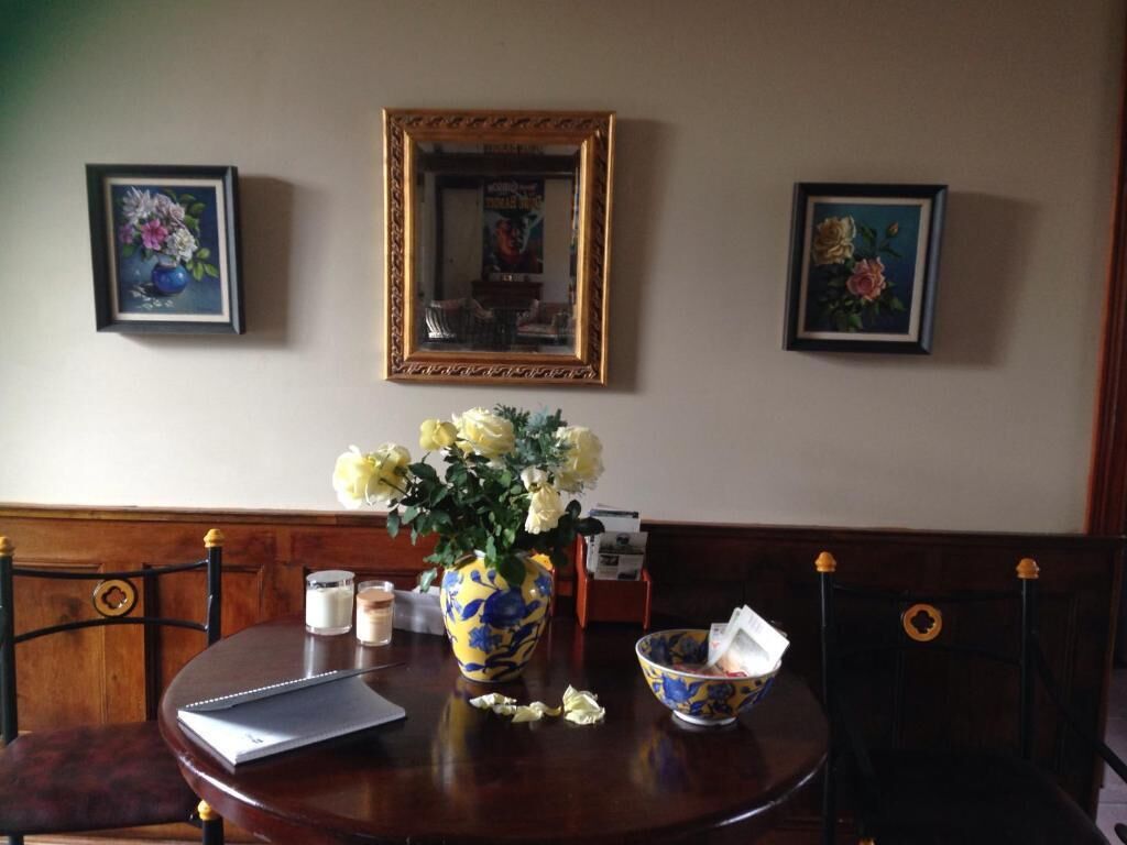 A dining table with a vase of flowers, a bowl, and a framed mirror on the wall.