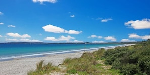 A beach with clear blue water, sandy shore, and green vegetation. - Gunyah - an idyllic coastal getaway (Callala Beach)