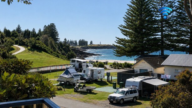 A campsite with RVs parked on a grassy area, a small building, and a view of the ocean. - Beachside Getaway - 150 metres to beach (Kiama)