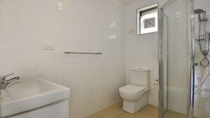 A bathroom with a white sink, toilet, and glass shower enclosure. - Beachside Getaway - 150 metres to beach (Kiama)