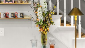 Una escalera con barandillas blancas, una mesa con un florero y una lámpara con pantalla dorada.