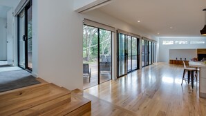 A spacious room with wooden flooring, large sliding glass doors leading to an outdoor area, and a modern kitchen area.