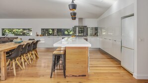 A modern kitchen with a central island, wooden dining table, and bar stools.