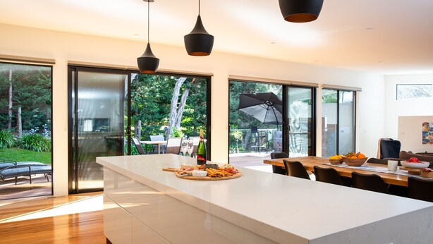 A modern kitchen with a large island, sliding glass doors leading to a patio, and a dining area with a wooden table and chairs.