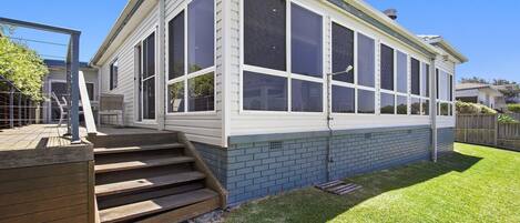 A house with a large covered patio, a brick foundation, and a set of wooden stairs leading to the entrance.