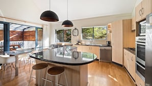 A modern kitchen with a central island, wooden cabinets, stainless steel appliances, and large windows.