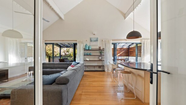 A spacious living area with a large grey sofa, a wooden dining table, and a kitchen area with a bar counter. - The River House - In the heart of Margaret River - idyllic getaway for families (Margaret River)