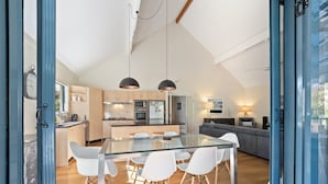A modern kitchen with a glass dining table and white chairs, a built-in oven, and a large window overlooking the city. - The River House - In the heart of Margaret River - idyllic getaway for families (Margaret River)