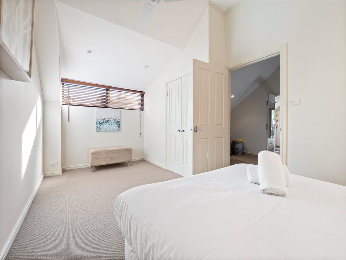 A bedroom with a large bed, a bench, a door, and a window with blinds.