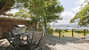 Une terrasse extérieure avec un barbecue, des chaises en bois et une vue sur les bateaux qui naviguent.