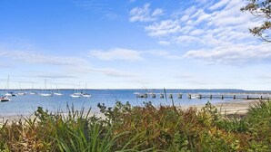 A coastal scene with sailboats docked at a pier, surrounded by grassy areas and a clear sky. - Bay Cottage – stunning water views of Callala Bay (Callala Bay)