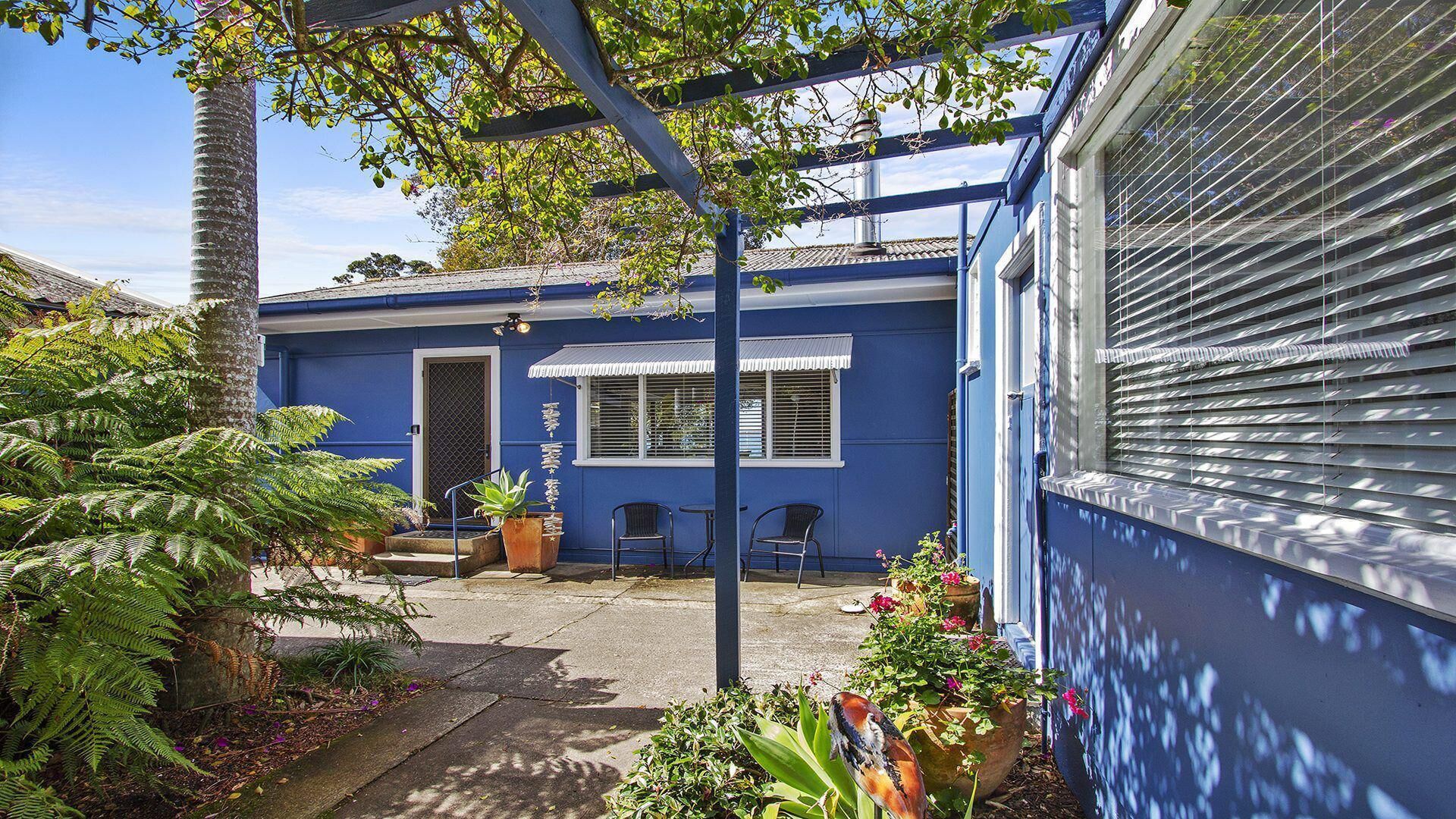 A blue house with a covered patio, two chairs, and potted plants.