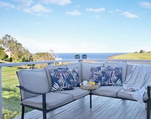 A deck with a grey sectional sofa, two patterned cushions, and a small round table with a tray.