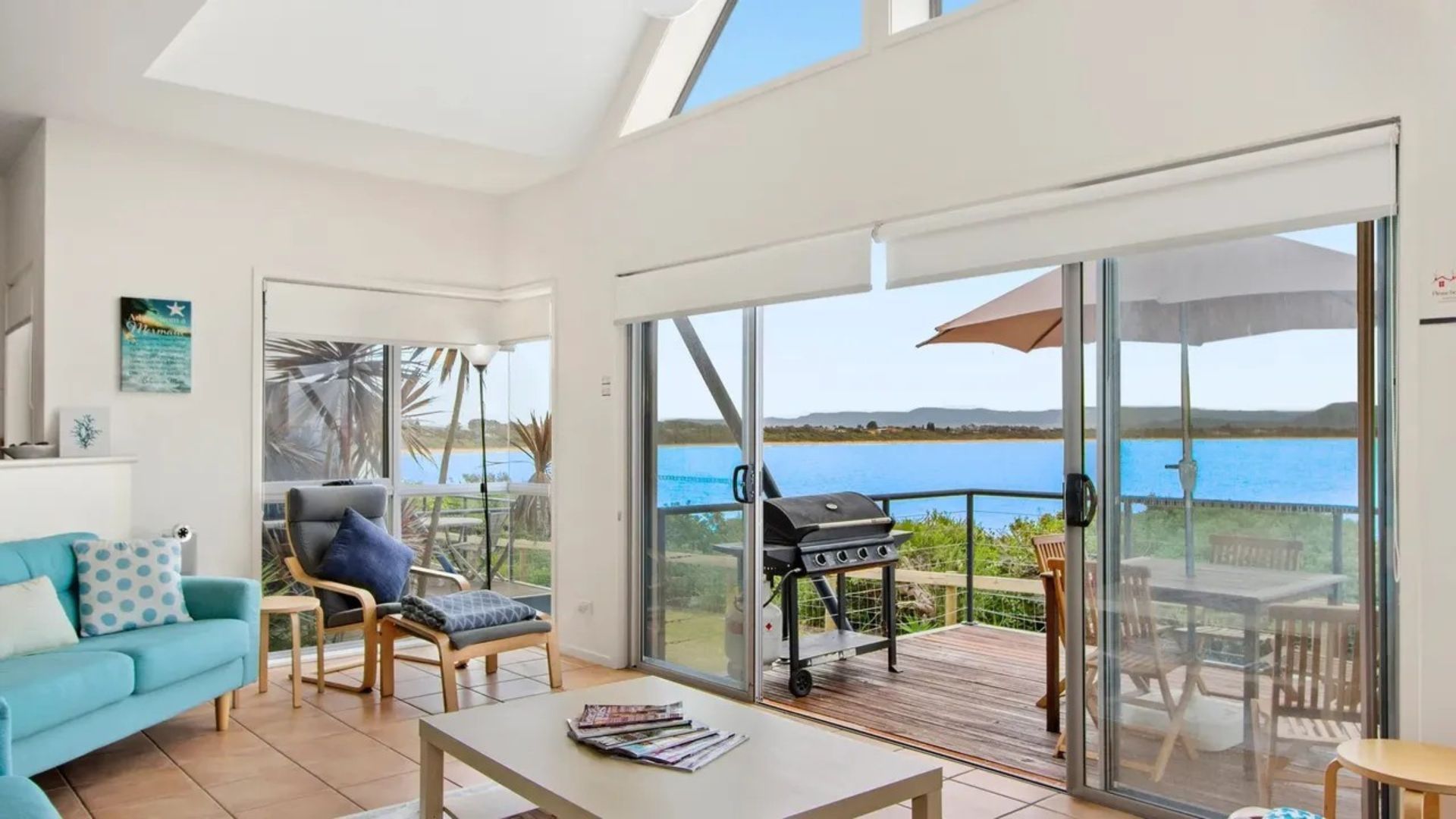 A spacious living area with a sofa, a chair, a table, and a grill outside a sliding glass door.