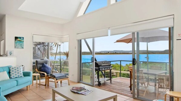 A spacious living area with a sofa, a chair, a table, and a grill outside a sliding glass door.