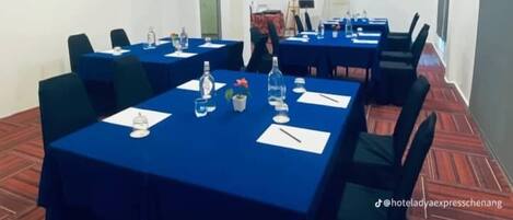 Een congreszaal met meerdere tafels, stoelen en een projecteerder aan het plafond.