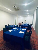 A conference room with multiple tables, chairs, and a projector on the ceiling.