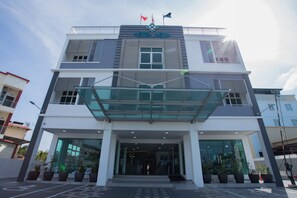 A modern hotel with a glass entrance, multiple floors, and a flag on top. - Adya Hotel Chenang (Langkawi)