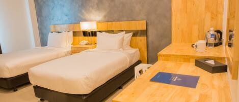 A hotel room with two beds, a wooden desk, a nightstand, a lamp, a phone, a water bottle, a coffee maker, and a framed picture on the wall.