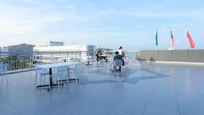 A rooftop terrace with white tables and chairs, flags, and a clear view of the cityscape. - Adya Hotel Chenang (Langkawi)