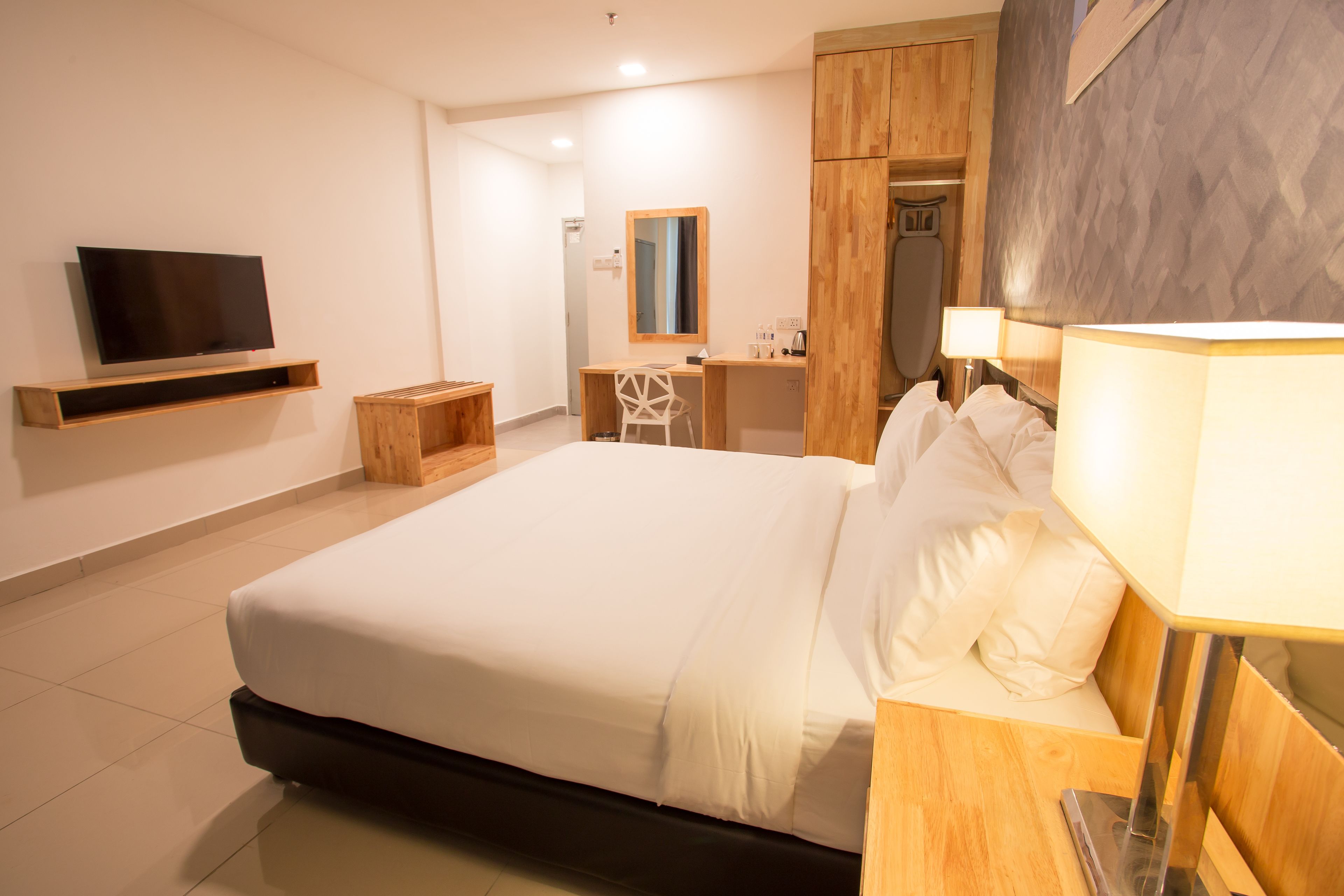 A modern hotel room with a large bed, a desk, a chair, a television, and a mirror.