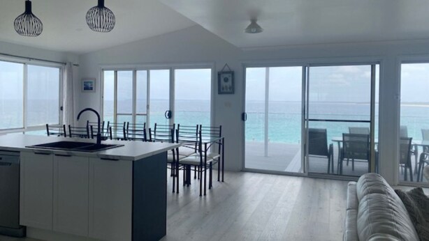 Una cocina amplia con una isla grande, un comedor con sillas y vistas al océano a través de puertas correderas.