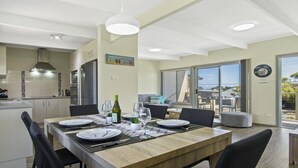 Un comedor moderno con una mesa de madera dispuesta para cuatro, una cocina al fondo y una puerta corrediza de vidrio que da a un patio exterior.
