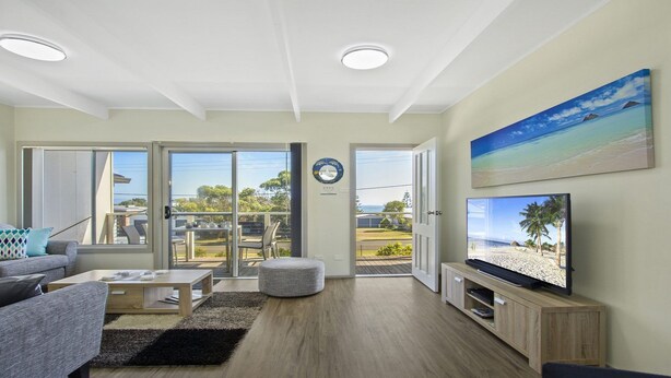 Amplia sala de estar con televisor grande, asientos cómodos y balcón con vistas.