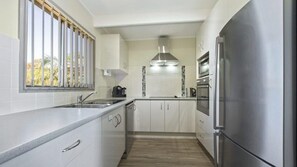 Enjoy cooking in this well-equipped kitchen with a stainless steel refrigerator, oven, and range hood.