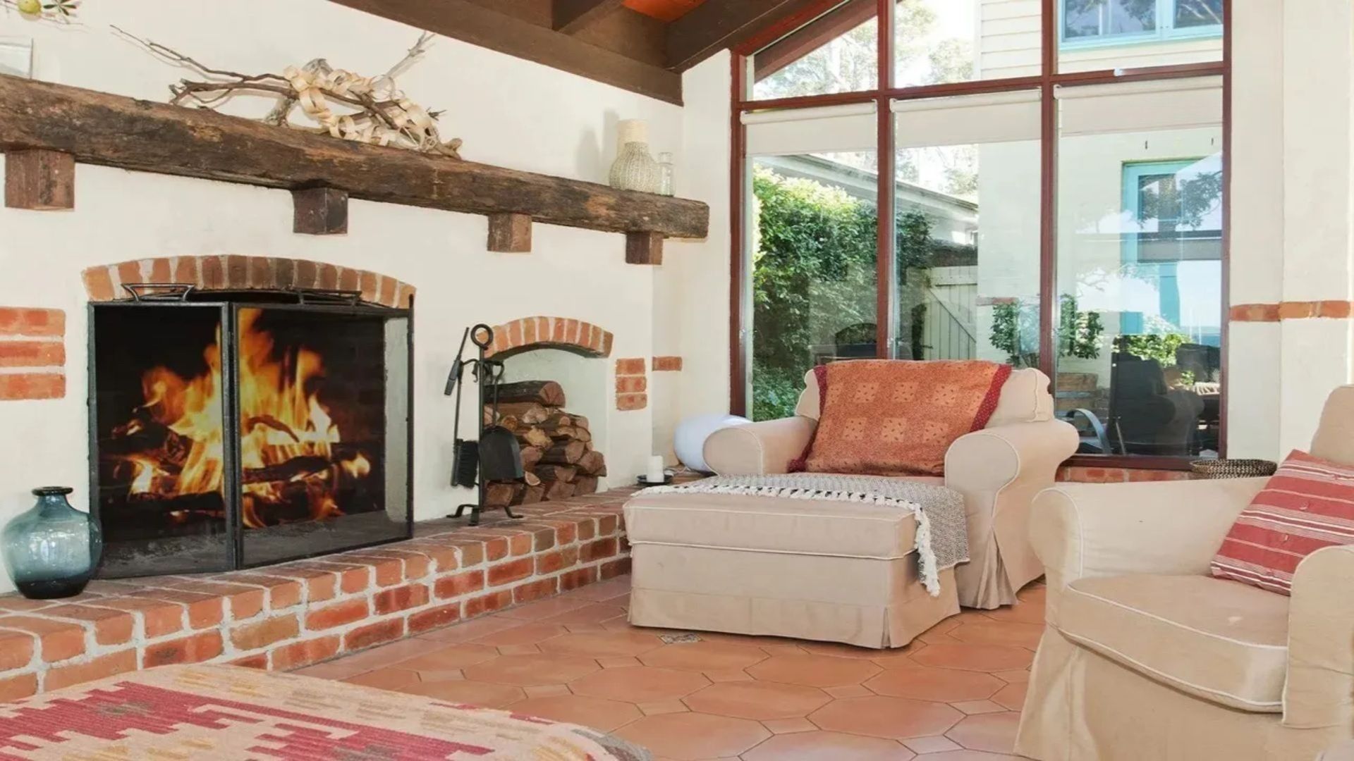 A cozy living room with a fireplace, a sofa, and a large window offering a view of the outdoors.