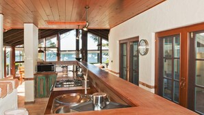 A kitchen with a wooden countertop, stainless steel sink, and a stove. There is a window overlooking a marina with boats. - Izba - on the foreshore of Callala Bay (Callala Bay)