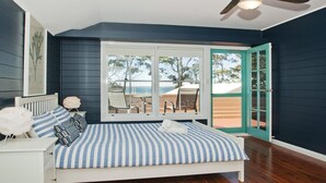 A bedroom with a bed, a nightstand, a clock, and a window with a view of the outdoors. - Izba - on the foreshore of Callala Bay (Callala Bay)