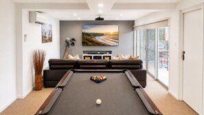 Una sala de estar moderna con una mesa de billar, un televisor de pantalla plana grande y un cuadro de paisaje.