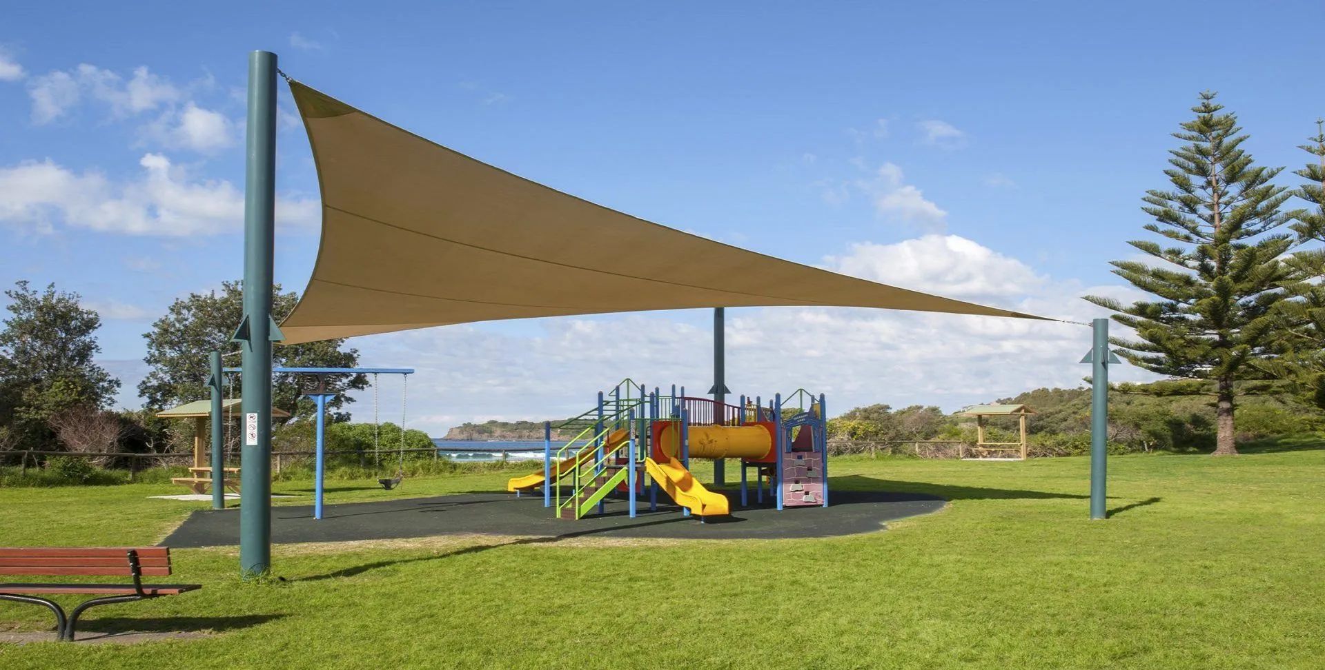 A playground with a beach access area, including slides and a swing set, under a large shade structure.