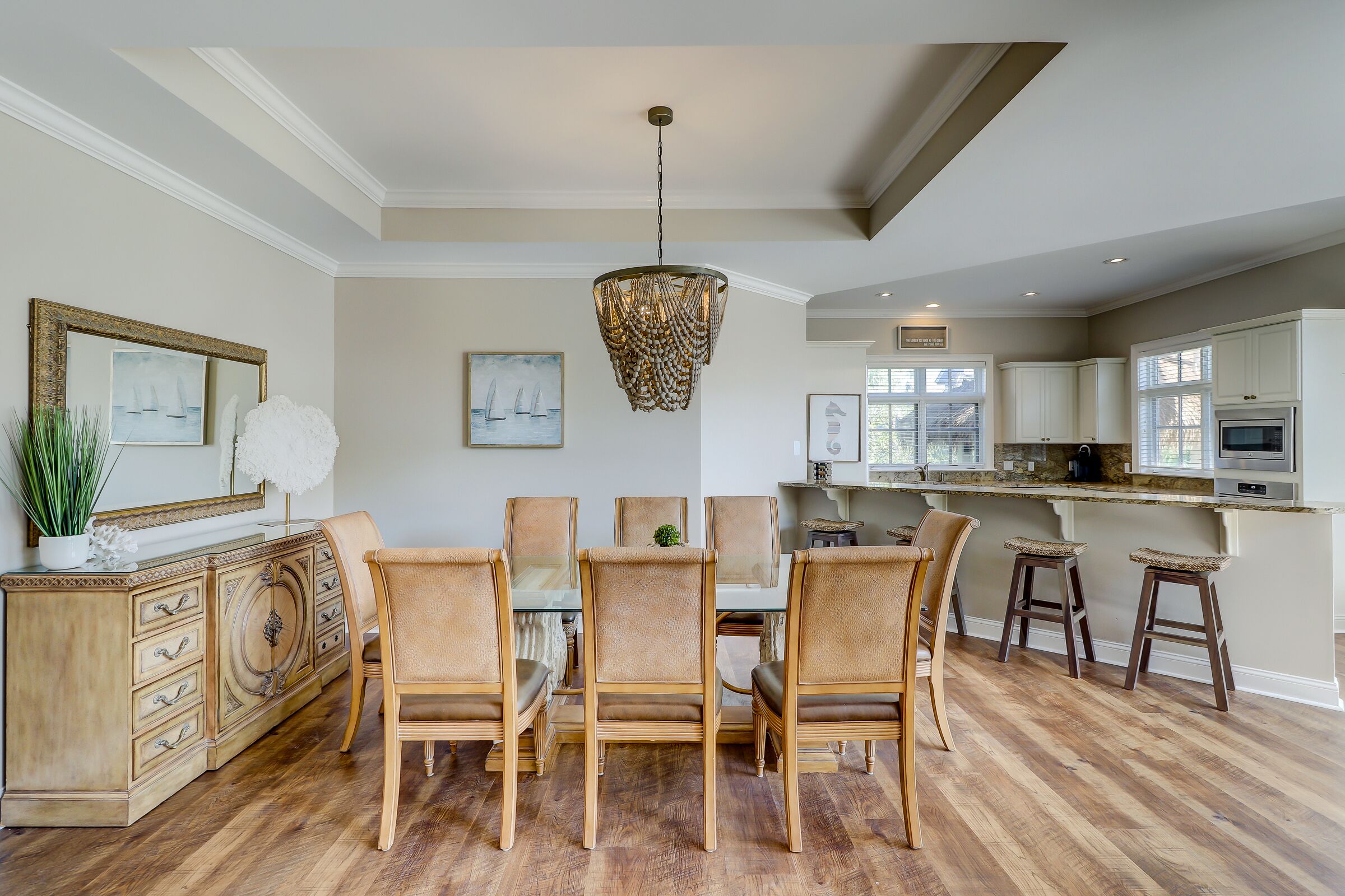 Un coin repas avec une table et des chaises en bois, un lustre et une cuisine en arrière-plan.