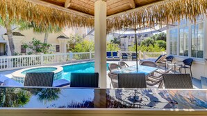 A covered outdoor area with a pool, lounge chairs, and a dining table. - 2nd Row luxury home with pool, tiki bar, private beach boardwalk- 30 Knotts Way (Hilton Head Island)