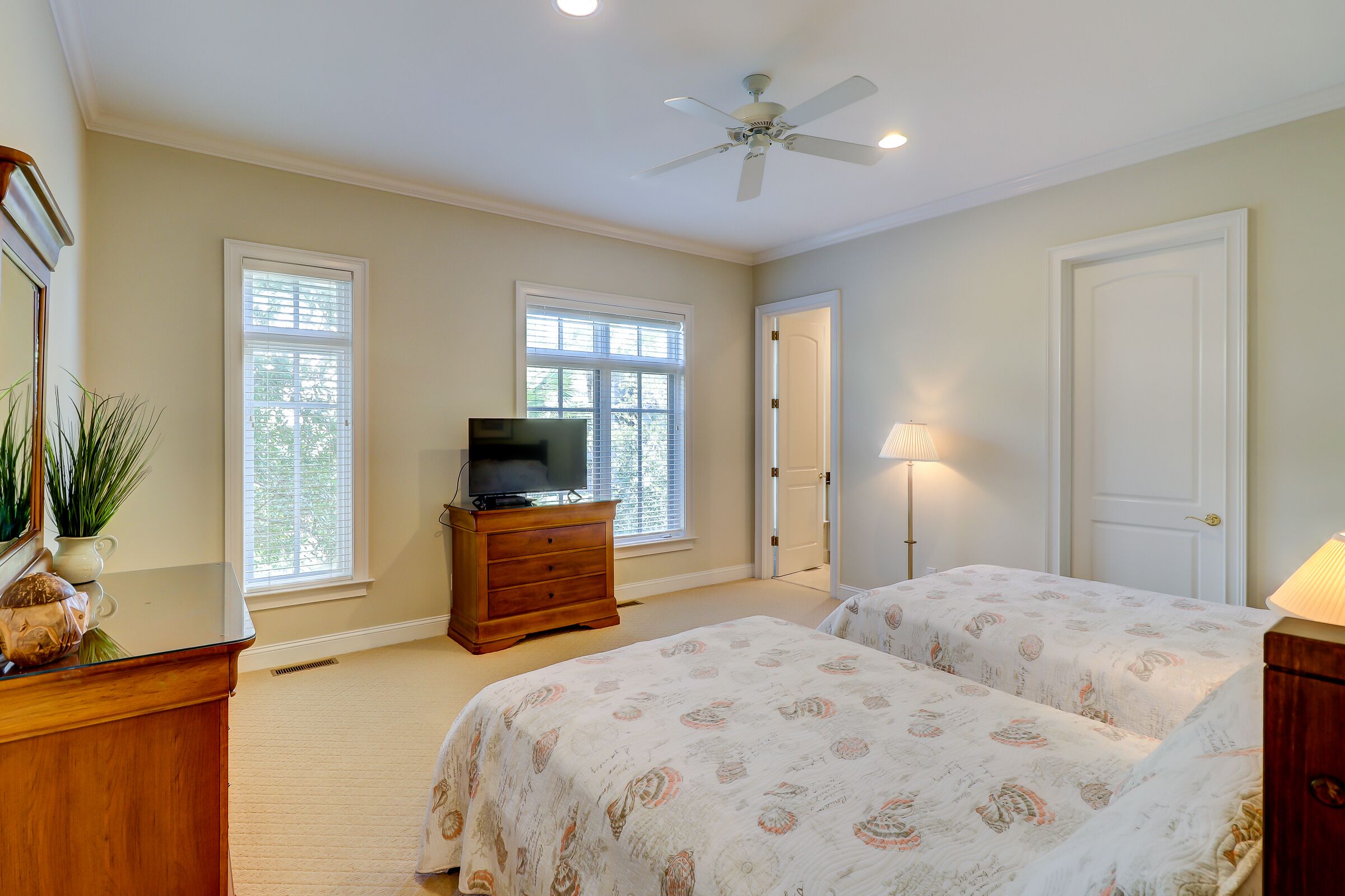 Une chambre avec deux lits, un téléviseur posé sur une commode en bois et un ventilateur de plafond.